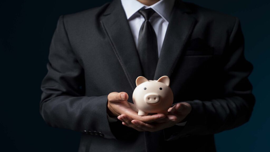 Businessman in suit holding pink piggy bank with both hands